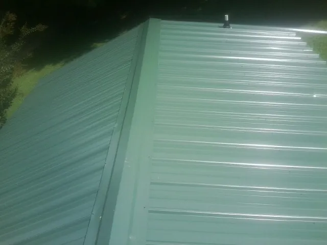 New green metal panels meeting at the ridge of a roof — Flat Roof Repair work by our crew in Port Monmouth