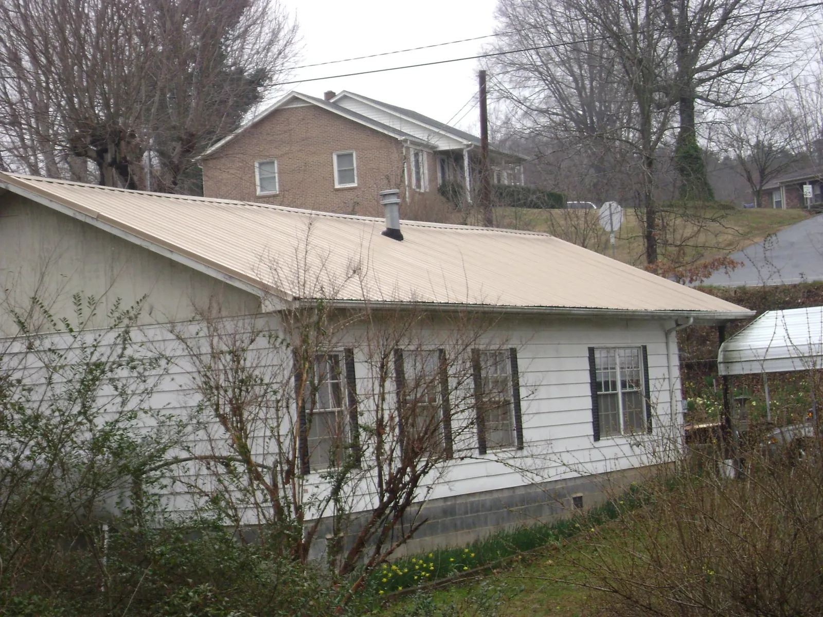 Tan metal roof on a white sided house set into a hillside — Commercial Roofing by Roofing Brothers in Port Monmouth